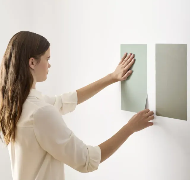 Applying two peel-and-stick paint samples to a white wall